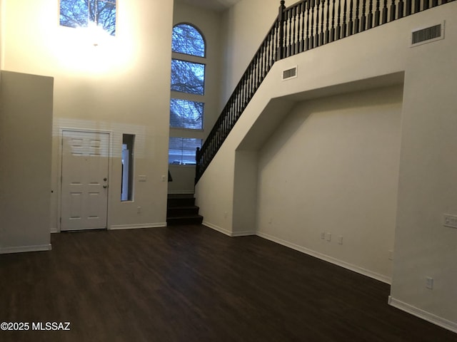 foyer entrance featuring visible vents, a towering ceiling, wood finished floors, baseboards, and stairs