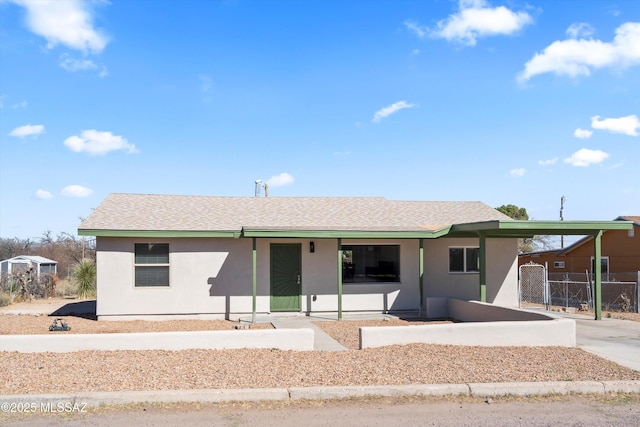 ranch-style home featuring a shingled roof, concrete driveway, an attached carport, fence, and stucco siding