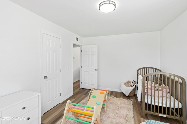 bedroom with a nursery area, baseboards, visible vents, and wood finished floors