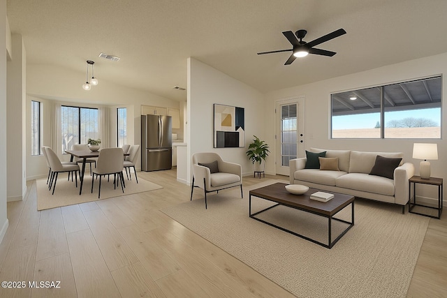 living room with visible vents, baseboards, a ceiling fan, light wood-style floors, and vaulted ceiling