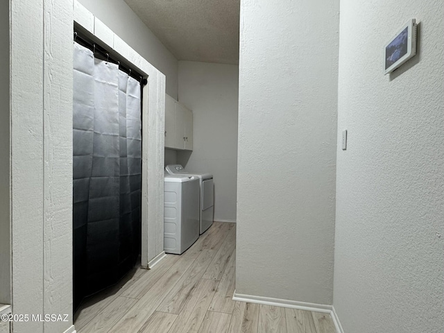 laundry room featuring light wood-style flooring, cabinet space, baseboards, washing machine and clothes dryer, and a textured wall