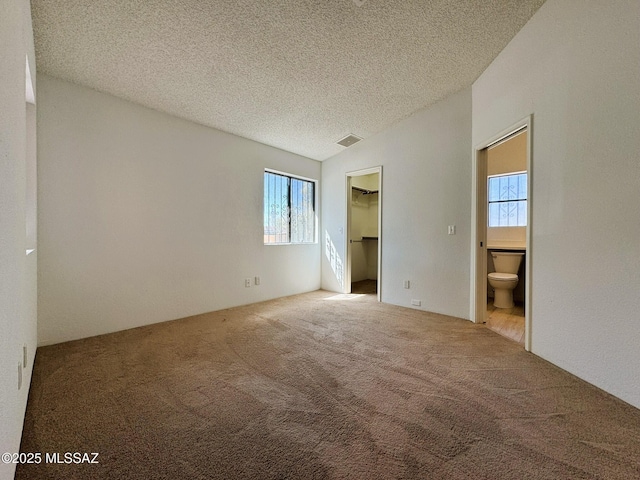 unfurnished bedroom featuring a textured ceiling, visible vents, carpet floors, vaulted ceiling, and a spacious closet