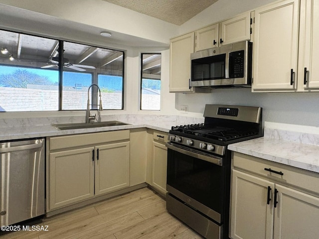 kitchen featuring a textured ceiling, light wood finished floors, light stone countertops, appliances with stainless steel finishes, and a sink