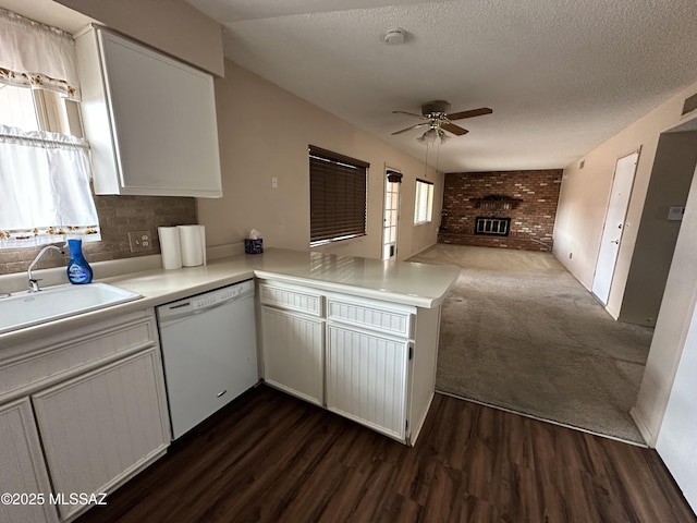 kitchen featuring light countertops, a brick fireplace, open floor plan, a sink, and dishwasher