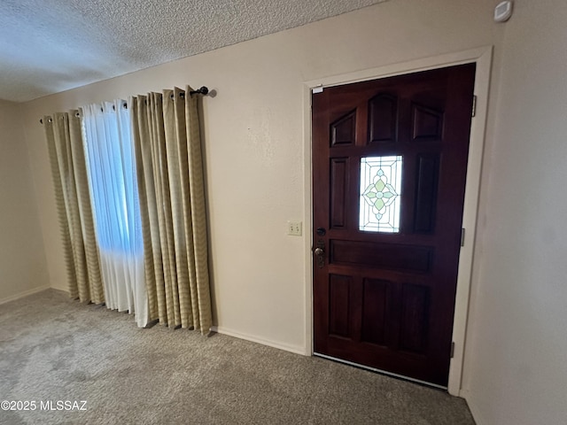 foyer entrance with a textured ceiling, carpet flooring, and baseboards