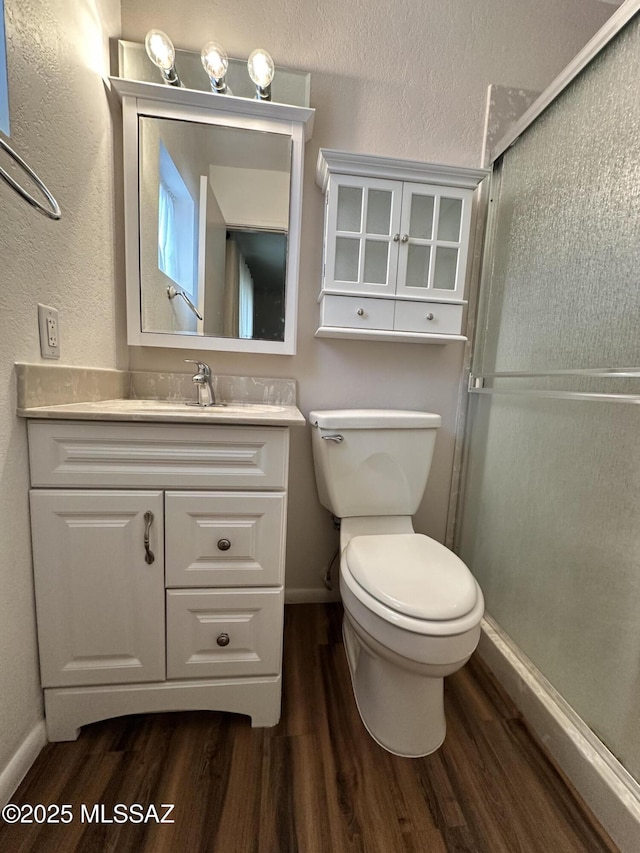 bathroom with toilet, vanity, a shower stall, wood finished floors, and baseboards