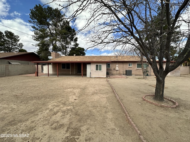 view of front of property with brick siding, a chimney, a patio area, central AC, and fence