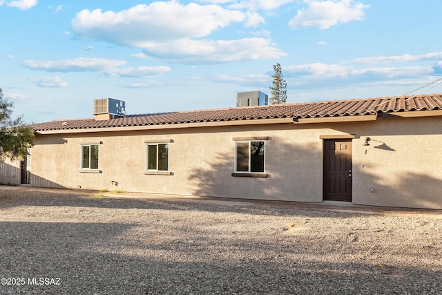 back of property featuring cooling unit, a tiled roof, and stucco siding