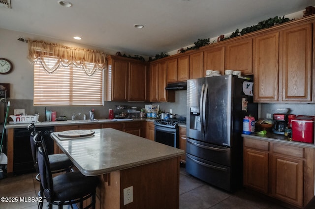 kitchen featuring tile patterned flooring, under cabinet range hood, stainless steel appliances, a kitchen island, and a kitchen breakfast bar
