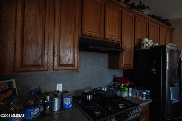 kitchen with stainless steel gas stove, fridge with ice dispenser, brown cabinets, and under cabinet range hood