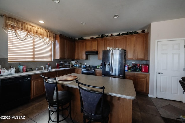kitchen featuring a center island, appliances with stainless steel finishes, a sink, dark tile patterned flooring, and under cabinet range hood