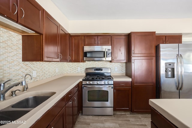 kitchen featuring wood finish floors, a sink, light countertops, appliances with stainless steel finishes, and backsplash