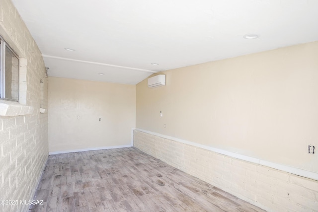 empty room with vaulted ceiling, an AC wall unit, brick wall, and wood finished floors