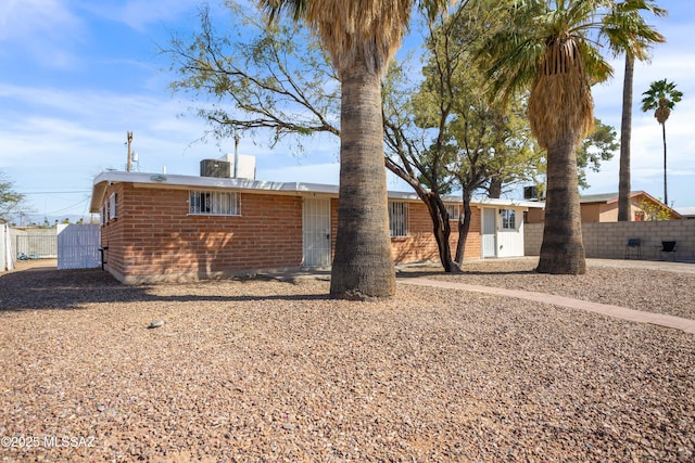 exterior space with cooling unit, brick siding, and fence