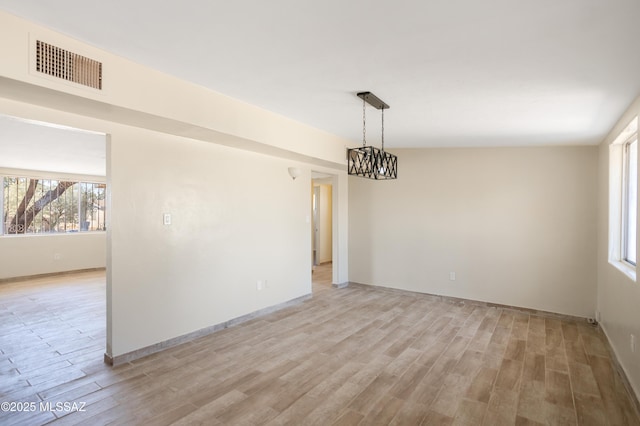 unfurnished room with light wood-type flooring, visible vents, and a chandelier