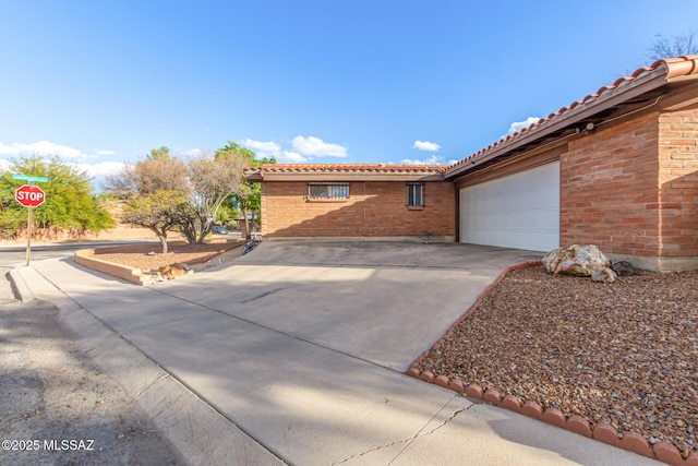 view of property exterior featuring a garage, driveway, brick siding, and a tile roof