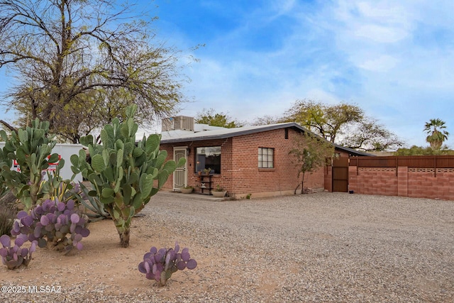 rear view of property with gravel driveway, fence, and brick siding