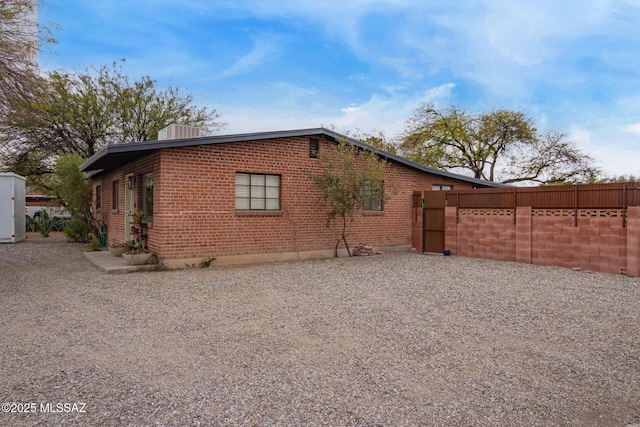 view of side of property with brick siding, central air condition unit, a gate, and fence