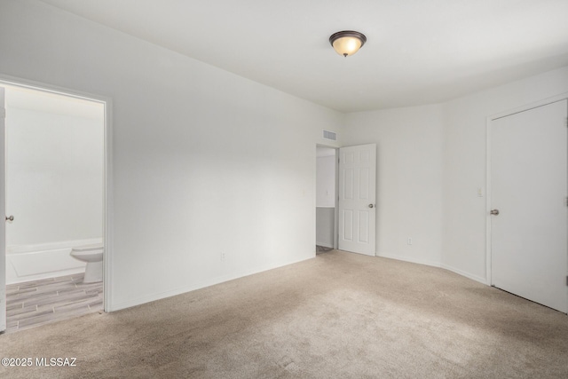 unfurnished bedroom with carpet flooring, connected bathroom, visible vents, and baseboards