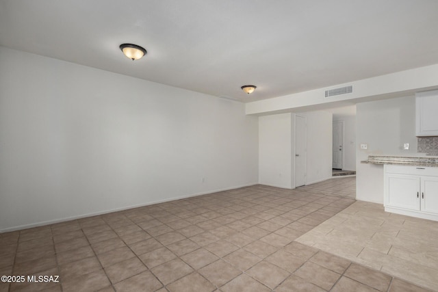 interior space with light tile patterned flooring, visible vents, and baseboards