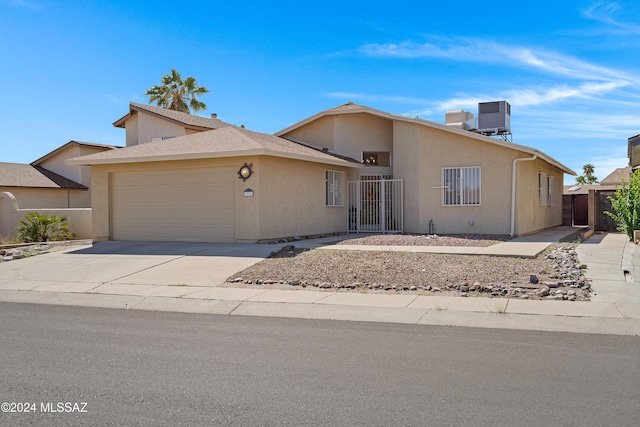 view of front facade with an attached garage, central air condition unit, fence, driveway, and stucco siding