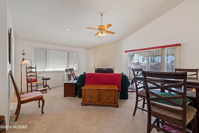 living area with light carpet, vaulted ceiling, a textured ceiling, and a ceiling fan