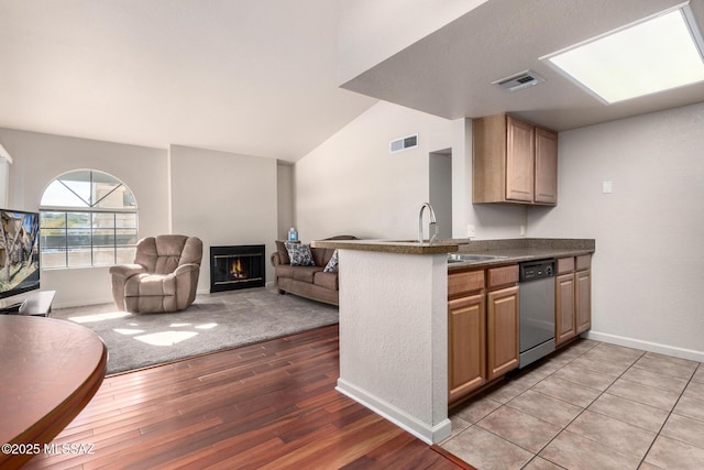 kitchen with light wood-style floors, dark countertops, dishwasher, a sink, and visible vents