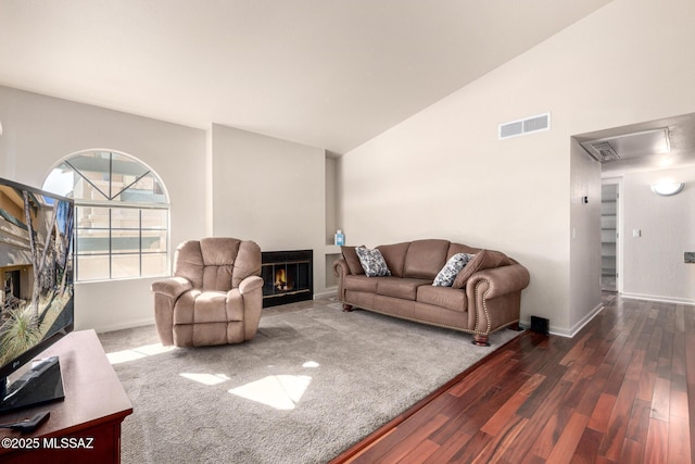 living room featuring visible vents, a lit fireplace, baseboards, vaulted ceiling, and wood finished floors