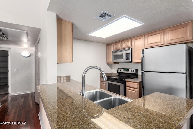 kitchen featuring light brown cabinets, stainless steel appliances, a sink, dark wood-style floors, and visible vents