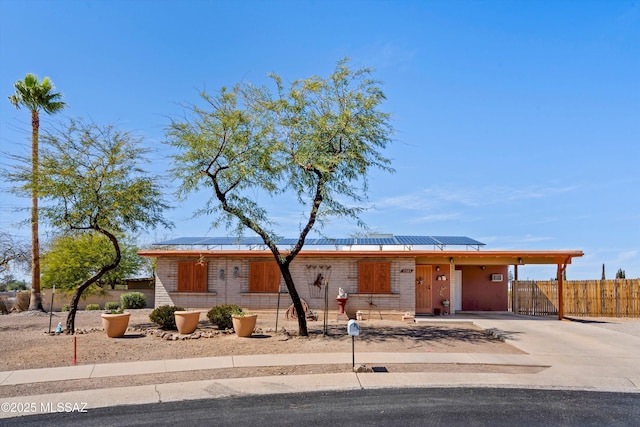 view of front of property featuring a carport, solar panels, concrete driveway, and fence