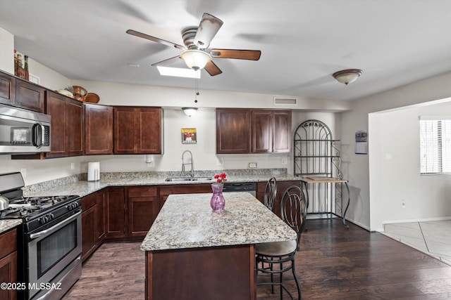 kitchen featuring a ceiling fan, a sink, stainless steel appliances, a breakfast bar area, and dark wood-style flooring