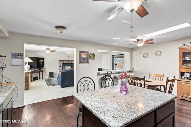 kitchen with wood finished floors, ceiling fan, a fireplace, and light stone countertops