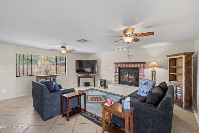 living room with a ceiling fan, visible vents, baseboards, light tile patterned flooring, and a brick fireplace