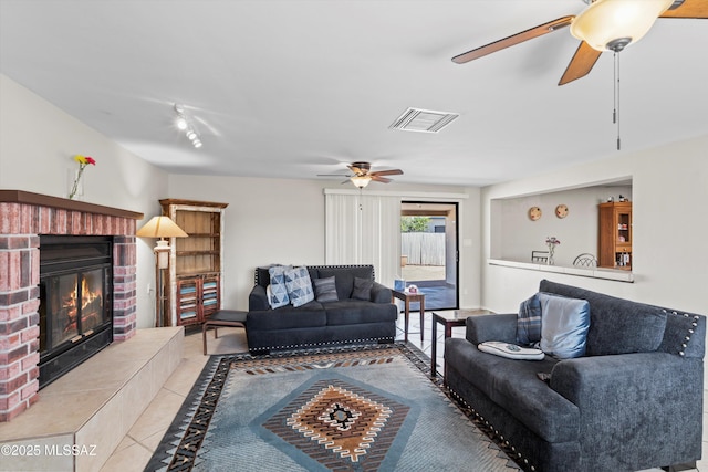 living area with tile patterned flooring, visible vents, a brick fireplace, and a ceiling fan