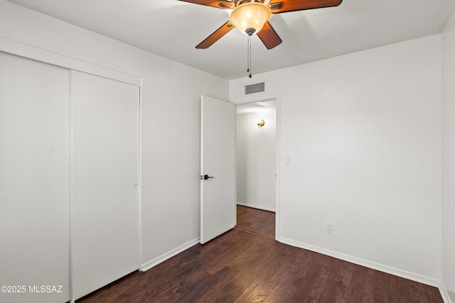 unfurnished bedroom with dark wood-style floors, visible vents, baseboards, ceiling fan, and a closet