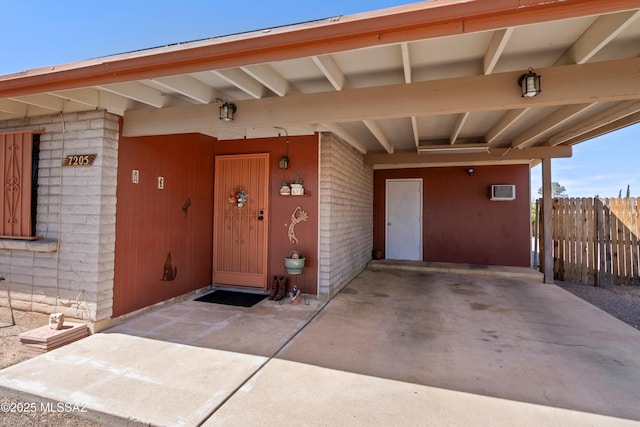 view of exterior entry featuring a carport, brick siding, and fence