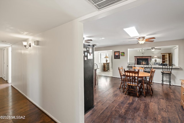 dining area featuring baseboards, visible vents, dark wood finished floors, ceiling fan, and a glass covered fireplace