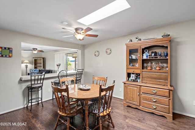 dining room featuring dark wood-type flooring, a skylight, a ceiling fan, and baseboards