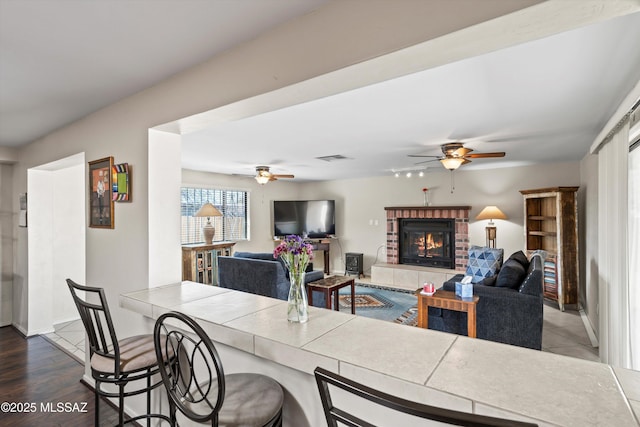 interior space with baseboards, dark wood-type flooring, a brick fireplace, and ceiling fan