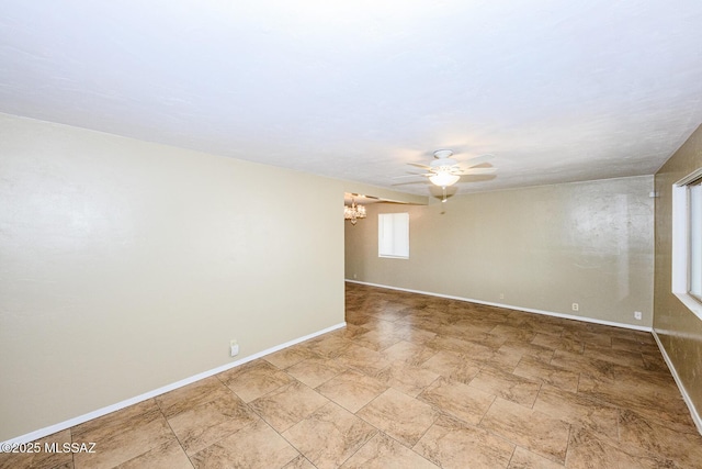 unfurnished room with baseboards and ceiling fan with notable chandelier