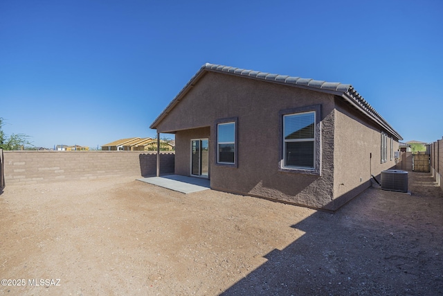 rear view of property with a tile roof, a patio, stucco siding, central AC unit, and a fenced backyard