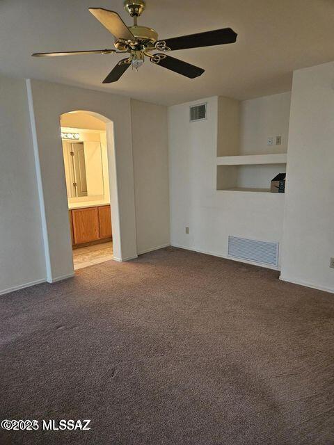 carpeted empty room featuring visible vents, arched walkways, and a ceiling fan