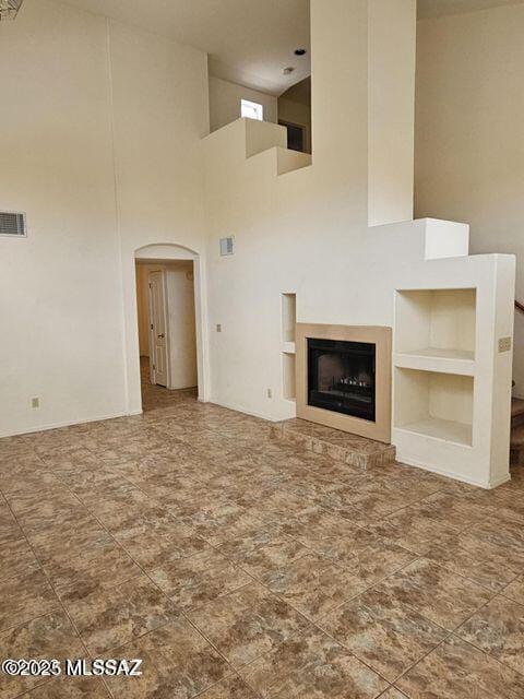 unfurnished living room with arched walkways, built in shelves, a fireplace, and visible vents