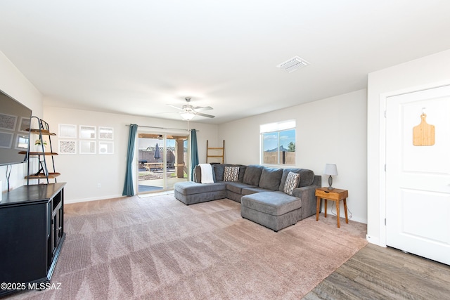 living room featuring light colored carpet, visible vents, light wood-style floors, ceiling fan, and baseboards