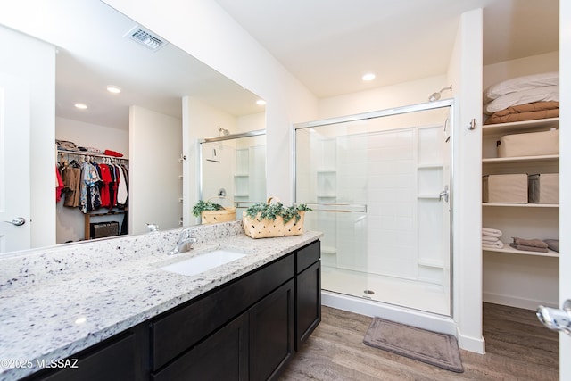 full bathroom featuring visible vents, a spacious closet, a stall shower, vanity, and wood finished floors