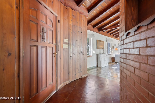 interior space with wooden walls, brick wall, vaulted ceiling with beams, wooden ceiling, and dark tile patterned floors