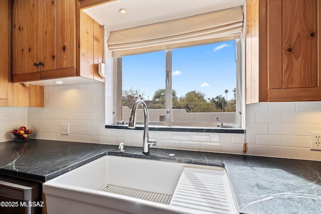 kitchen with brown cabinetry, decorative backsplash, dark countertops, and a sink