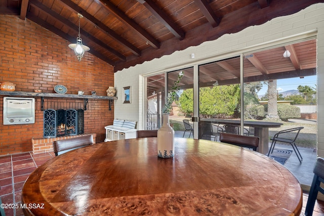 dining area featuring lofted ceiling with beams, wooden ceiling, brick wall, and an outdoor brick fireplace