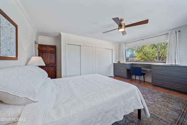 bedroom with dark tile patterned floors, a ceiling fan, multiple closets, and ornamental molding