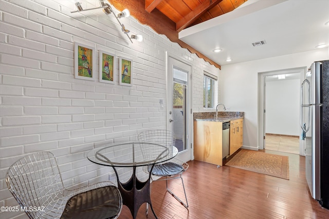 kitchen featuring light wood-type flooring, beamed ceiling, visible vents, stainless steel appliances, and brick wall